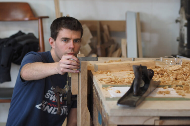 A furniture making student using a square with a plane.