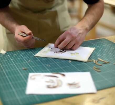 A photo from the Marquetry Course at Farnham School of Furniture Making. It shows a pupil cutting a stencil of some detailed marquetry.